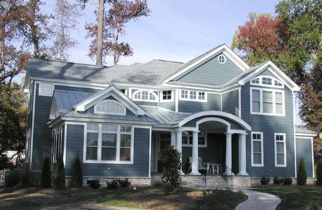 Two-story blue house with white trim, arch-top windows, a large front porch, a shingled roof, and a paved walkway.