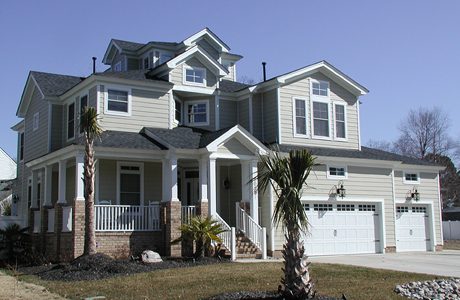 A large two-story home with gray siding, white trim, a double garage, and two small palm trees in front.